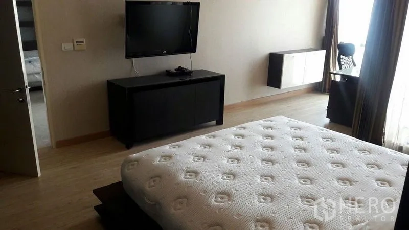 Condominium for rent in Khlong Luang, Pathum Thani - Master bedroom with mounted TV, low cabinet, wood flooring and large window.