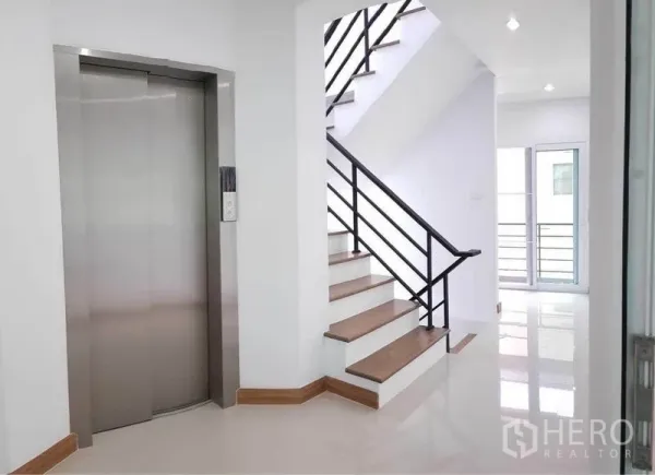 带办公室的家 出租在Prawet, Bangkok - 楼梯与不锈钢电梯特写，洁白室内并连通小阳台的玻璃门。