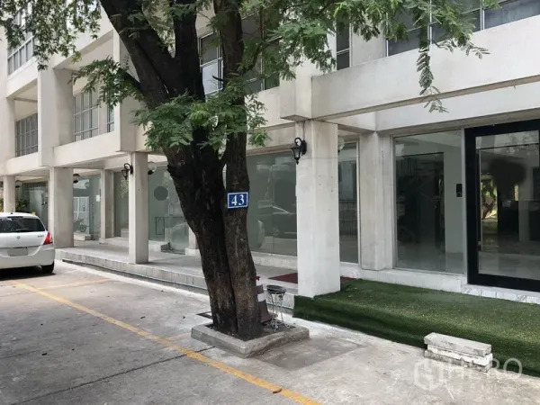 零售空间 出租在Watthana, Bangkok - 现代玻璃立面商业建筑，设有停车位与行道树。