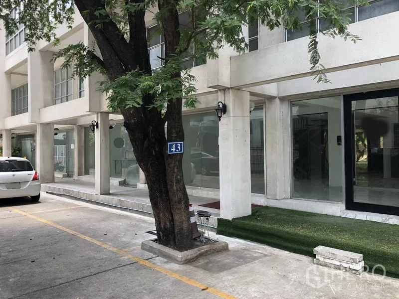 零售空间 出租在Watthana, Bangkok - 现代玻璃立面商业建筑，设有停车位与行道树。