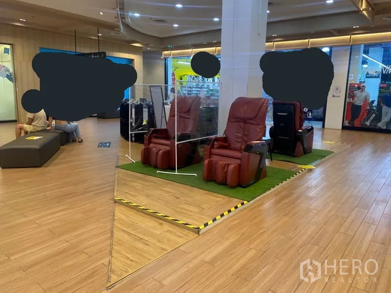 零售空间 出租在Khlong Toei, Bangkok - 角落零售位，抬高平台上的按摩椅，木地板与吊顶照明的商场环境。