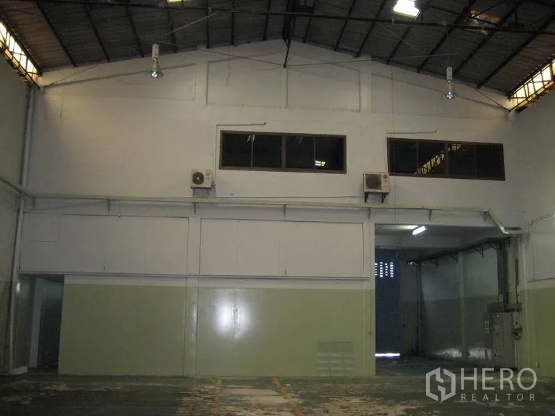 Factory for rent in Bang Sao Thong, Samut Prakan - Loading bay entrance with roller shutter, mezzanine windows, and exterior AC units.