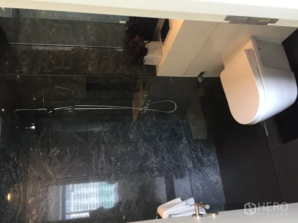 公寓 出售在Bang Rak, Bangkok - 现代卫浴，深色石材墙面，玻璃淋浴间与挂墙式马桶。