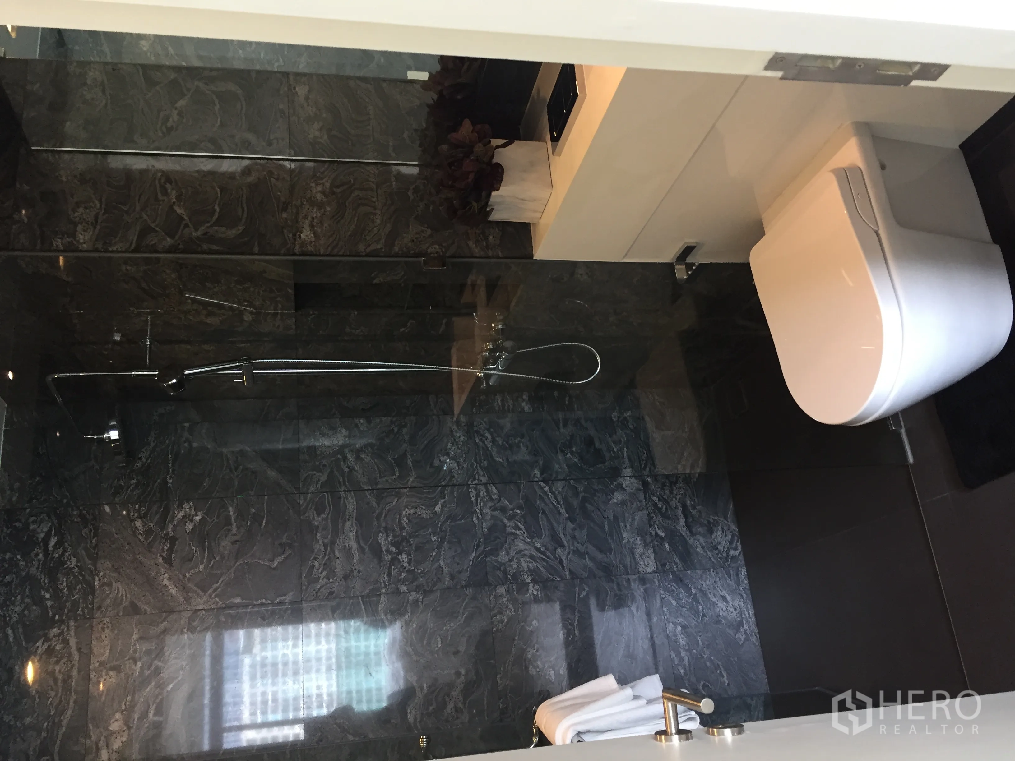 公寓 出售在Bang Rak, Bangkok - 现代卫浴，深色石材墙面，玻璃淋浴间与挂墙式马桶。