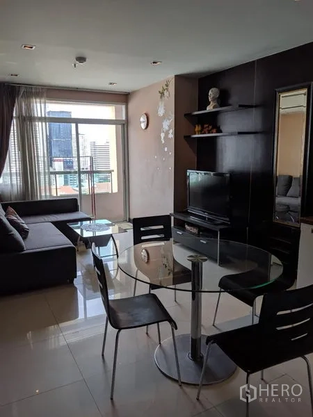 Condominium for rent in Watthana, Bangkok - Open-plan living and dining area with sofa, TV wall, balcony access and round glass table.