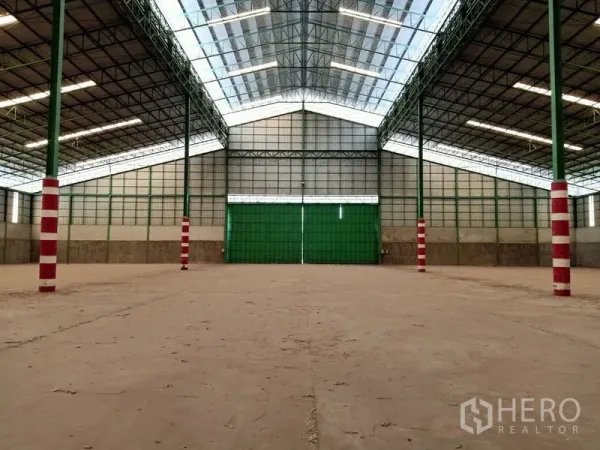 Factory for rent in Chaloem Phra Kiat, Saraburi - Clear‑span warehouse hall featuring wide green sliding doors and natural light panels under a gabled roof.