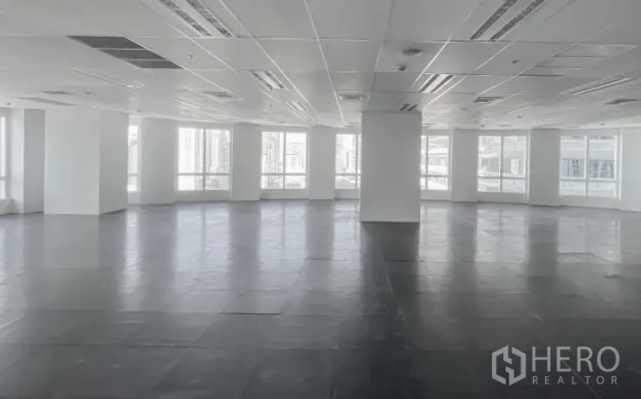 Office Space for rent - Bright corner office floor plate with columns, grid ceiling, and large windows overlooking the skyline.