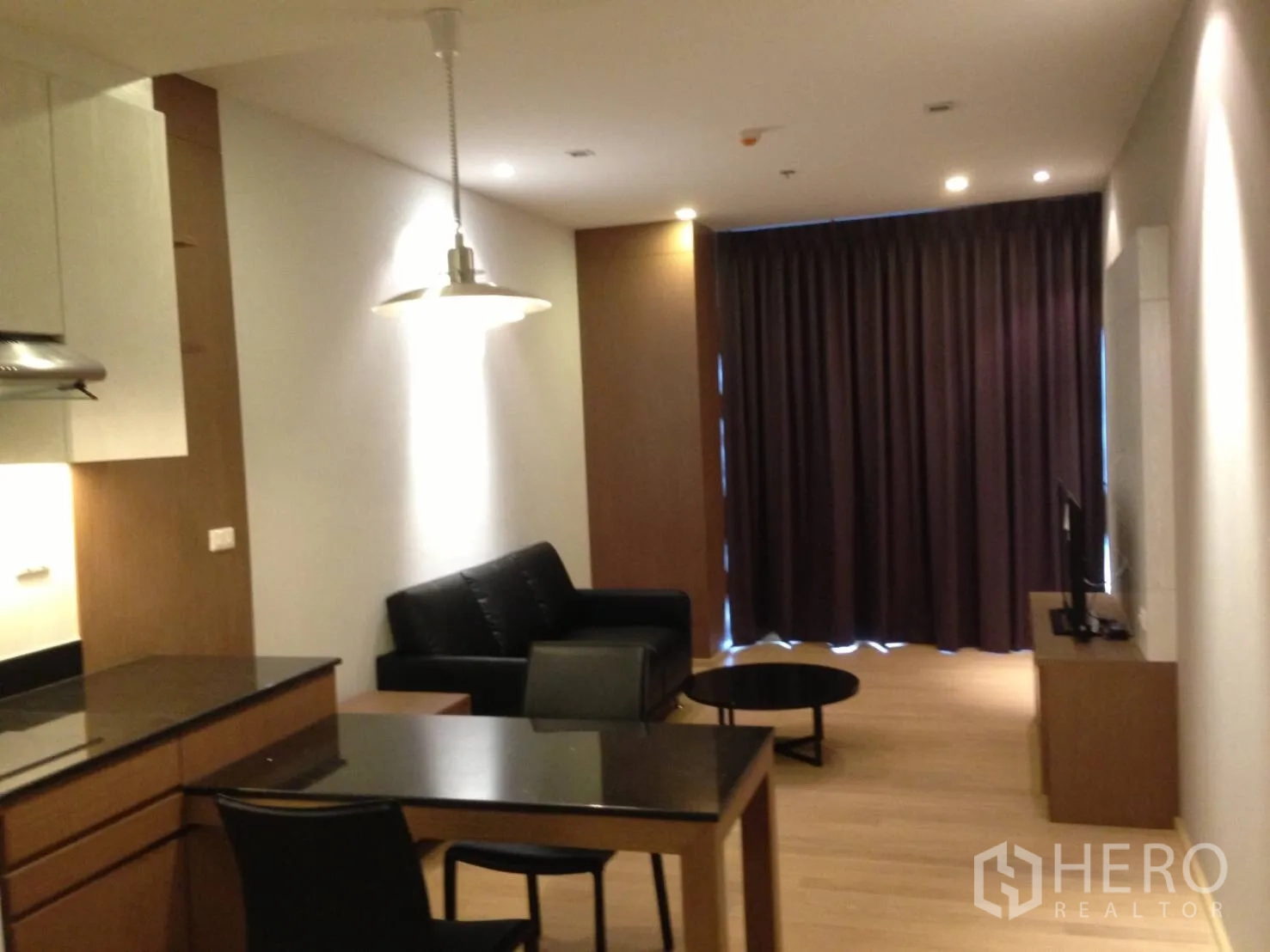 คอนโด ให้เช่าในBangkok - พื้นที่นั่งเล่นและรับประทานอาหารแบบเปิดในคอนโดคลองเตย พร้อมครัวบิลท์อิน โคมไฟ โซฟาสีดำ และผ้าม่านทึบ