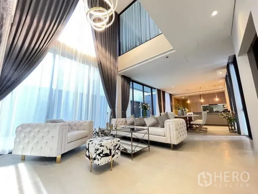 Detached House for sale in Suan Luang, Bangkok - Double-height living room with floor-to-ceiling curtains, modern chandelier and tufted sofas opening to the dining area.