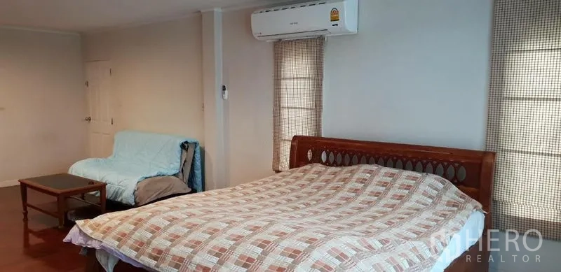 บ้าน ให้เช่าในPhra Khanong, Bangkok - ห้องนอนกว้าง เตียงไม้ ผ้าห่มลายตาราง แอร์ผนัง โซฟาและโต๊ะเล็ก ข้างหน้าต่างพร้อมผ้าม่าน