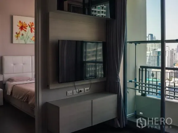 คอนโด ให้เช่าในRatchathewi, Bangkok - ผนังติดทีวีใกล้ประตูกระจกบานเลื่อน เปิดออกสู่ระเบียงวิวเมือง