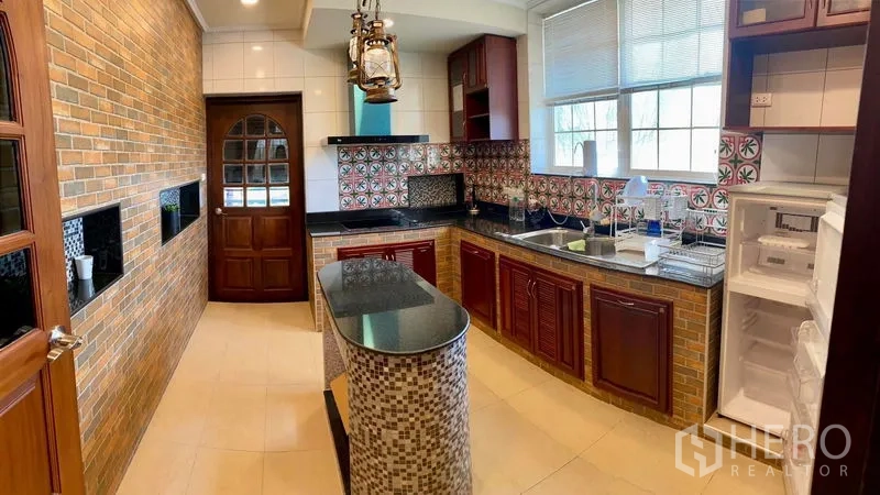 Detached House for sale in Bang Bo, Samut Prakan - Closed kitchen with island, granite counters, brick accents, and patterned backsplash.