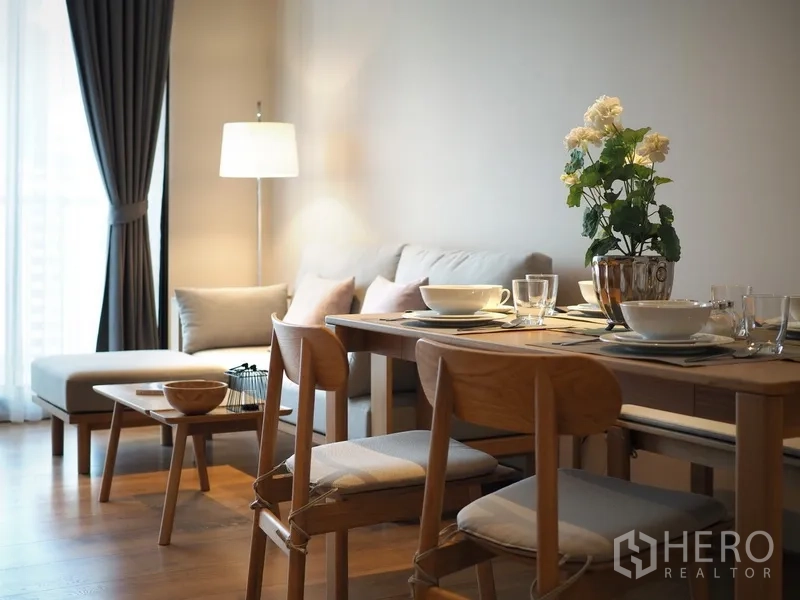 Condominium for sale in Khlong Toei, Bangkok - Close-up of the dining table and lounge with an L-shaped sofa, floor lamp and sheer curtains.
