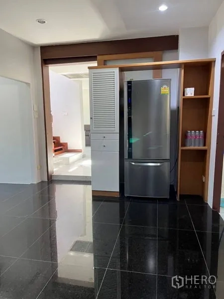 独立式住宅 出租在Samut Prakan - 厨房区域设高柜与冰箱位，黑色亮面地砖。