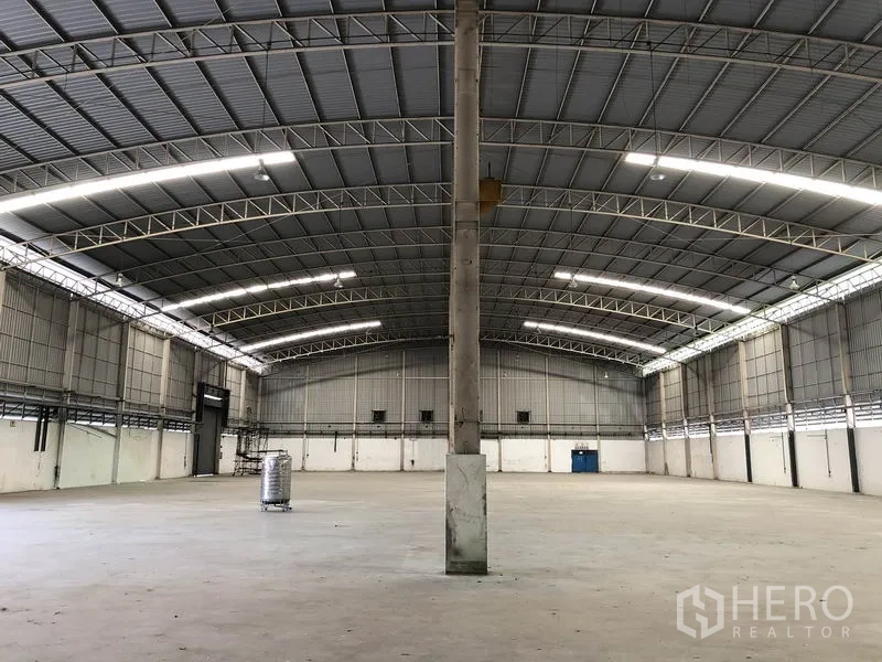 工厂 出租在Phra Nakhon Si Ayutthaya - 开放式厂房地面，中央立柱与弧形桁架屋顶，线性照明明亮。