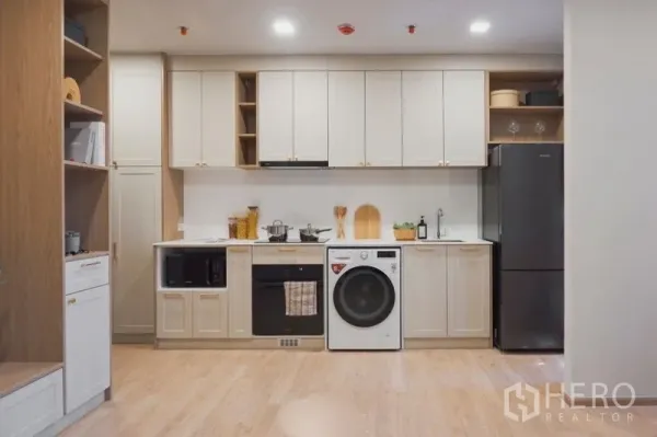 Condominium for sale in Suan Luang, Bangkok - Full-length kitchen wall with oven, microwave, washer and refrigerator over light wood flooring.