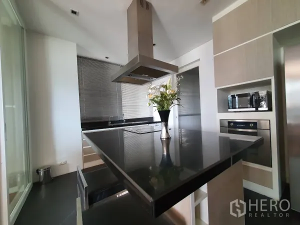 Condominium for rent in Khlong Toei, Bangkok - Modern separate kitchen featuring a black island, range hood and light wood cabinetry.