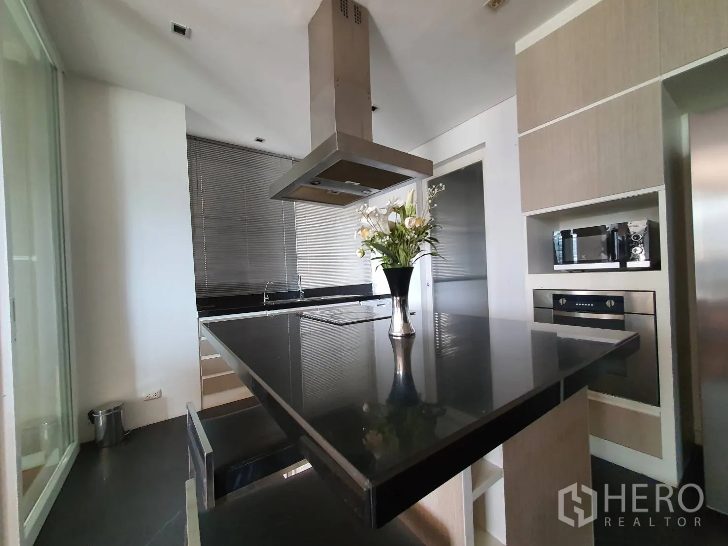 Condominium for rent in Khlong Toei, Bangkok - Modern separate kitchen featuring a black island, range hood and light wood cabinetry.