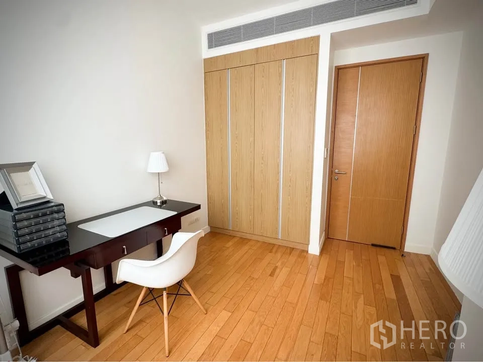 คอนโด for rent or sale in Khlong Toei, Bangkok - ห้องทำงานหรือห้องนอนพร้อมโต๊ะทำงาน เก้าอี้สีขาว และตู้เสื้อผ้าบิวท์อิน พื้นไม้.