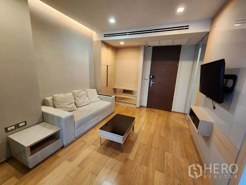 Condominium for sale in Ratchathewi, Bangkok - Modern living area by the entry with beige sofa, TV unit and light wood flooring.