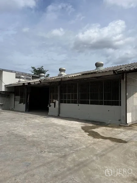 คลังสินค้า ให้เช่าในBangkok - ภายนอกโกดังชั้นเดียว มีพัดลมระบายอากาศบนหลังคา และลานคอนกรีตกว้าง