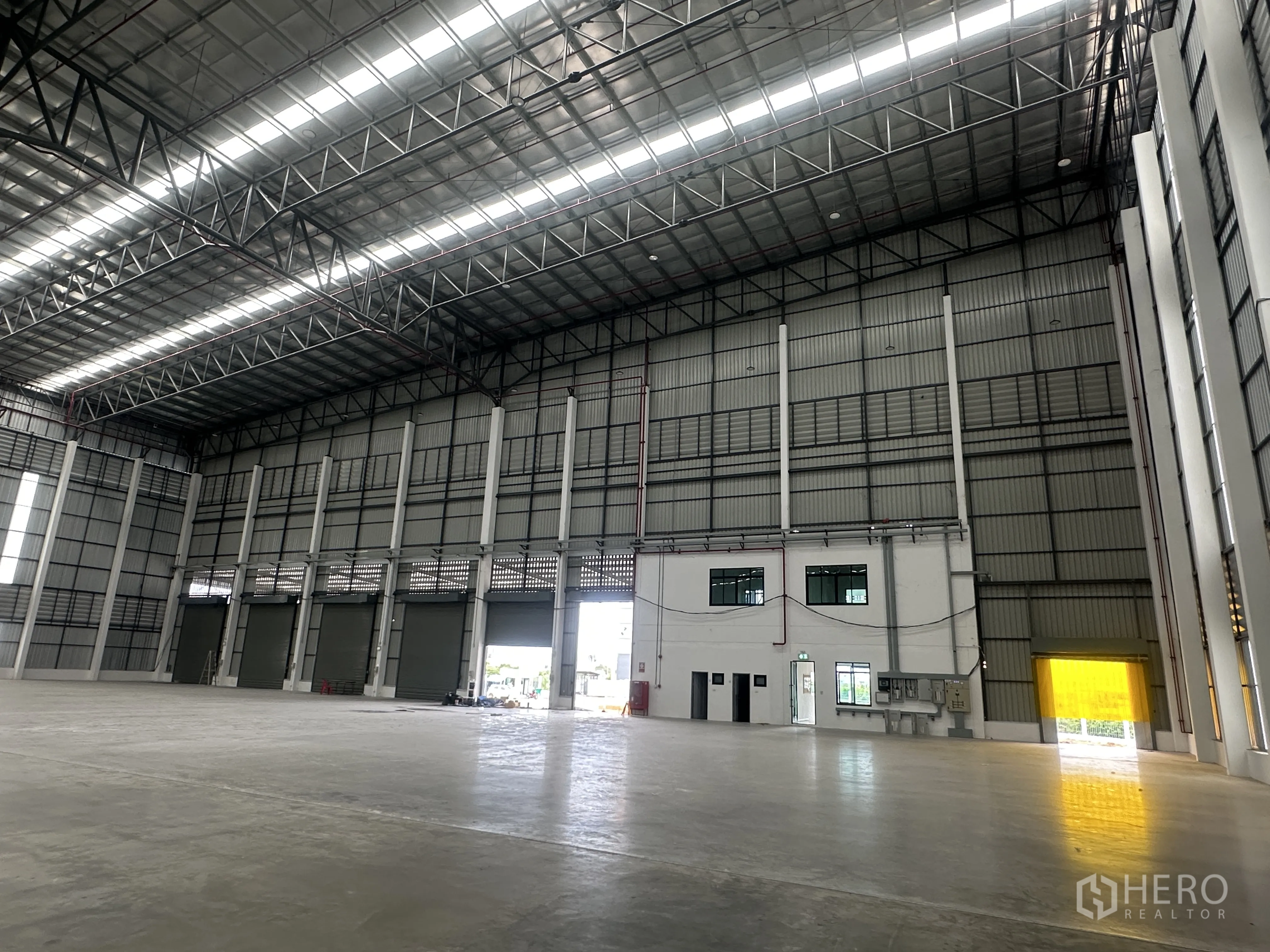 Factory for rent in Bang Phli, Samut Prakan - Interior loading zone with multiple roller shutter doors and an attached two-storey office.
