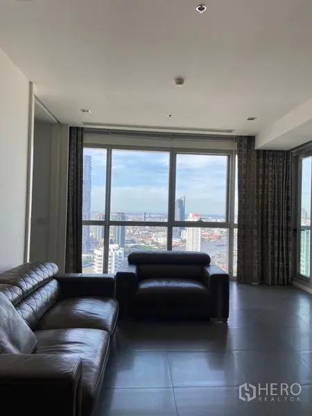 Condominium for sale in Khlong San, Bangkok - Bright living room with leather sofas and floor-to-ceiling windows overlooking the Chao Phraya River and Bangkok skyline.