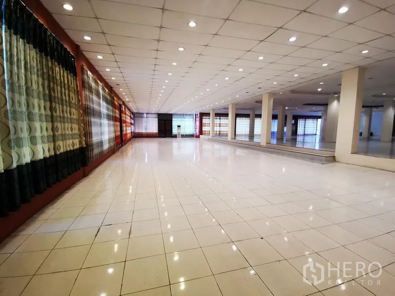 Retail Space for rent in Lam Luk Ka, Pathum Thani - Long open‑plan sales floor with full‑height windows, bright ceiling lighting and glossy white tiles.