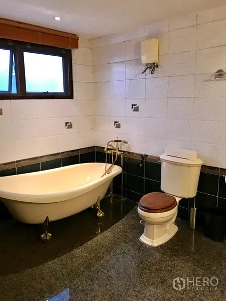 Condominium for rent in Bang Rak, Bangkok - Spacious bathroom with freestanding bathtub, toilet and window above tiled walls.