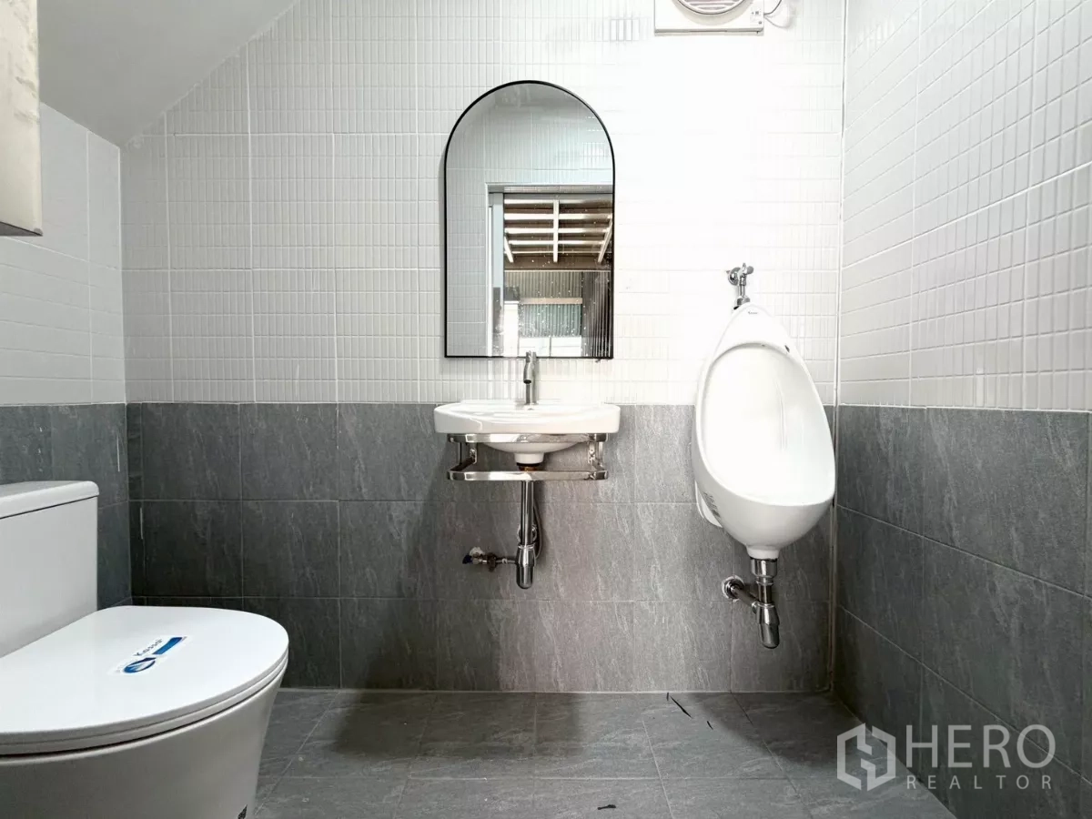 货栈 出租在Suan Luang, Bangkok - 仓库内的整洁卫生间，坐便器、小便斗、洗手盆与镜子，墙面瓷砖。