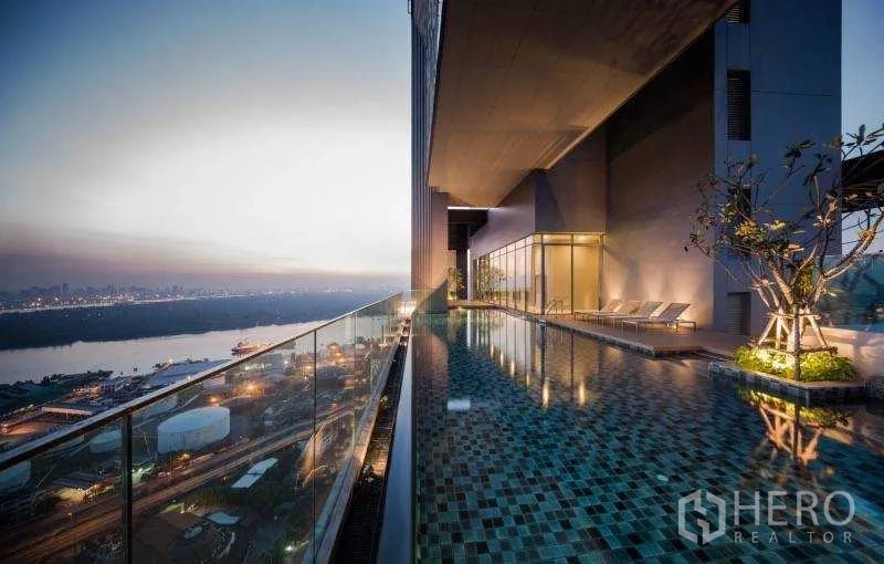Condominium for rent or sale in Bang Rak, Bangkok - Long elevated swimming pool with glass railing overlooking the city and river lights in the evening.