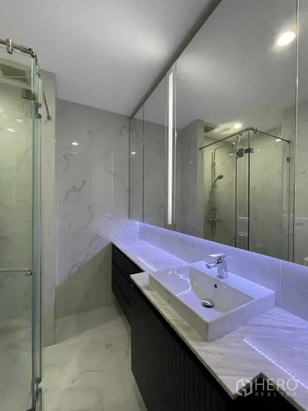 Condominium for rent in Pathum Wan, Bangkok - Second bathroom with marble walls, illuminated mirror, vessel sink and glass shower.