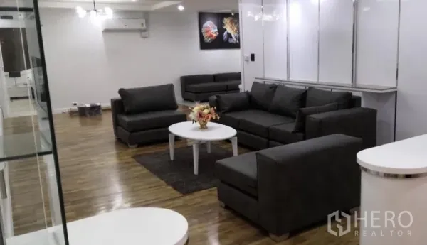 คอนโด ให้เช่าในKhlong Toei, Bangkok - ห้องนั่งเล่นกว้างพร้อมโซฟาผ้าสีเทา โต๊ะกลางสีขาว พื้นไม้ และภาพตกแต่งผนัง