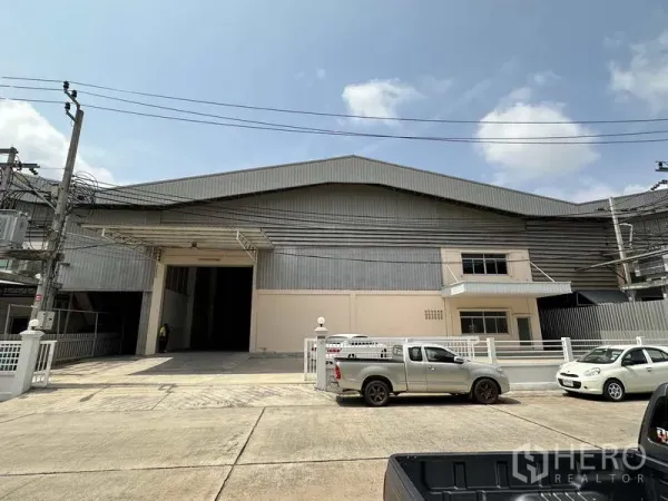 工厂 出租在Samut Prakan - 工厂正立面，宽大装卸入口、围栏与混凝土前院。