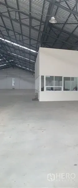 Warehouse for rent in Phra Pradaeng, Samut Prakan - Interior corner office with windows overlooking the warehouse floor beneath a metal roof structure.