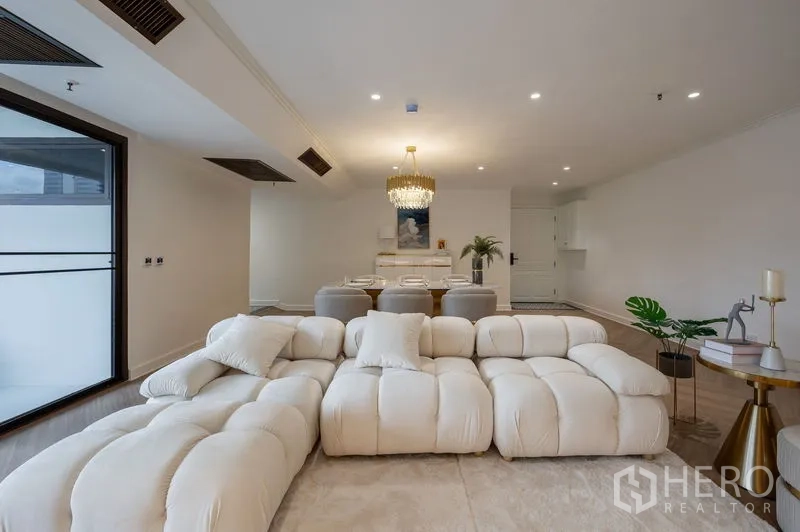 Condominium for sale in Watthana, Bangkok - Spacious lounge with an oversized sectional sofa facing the dining zone and chandelier.