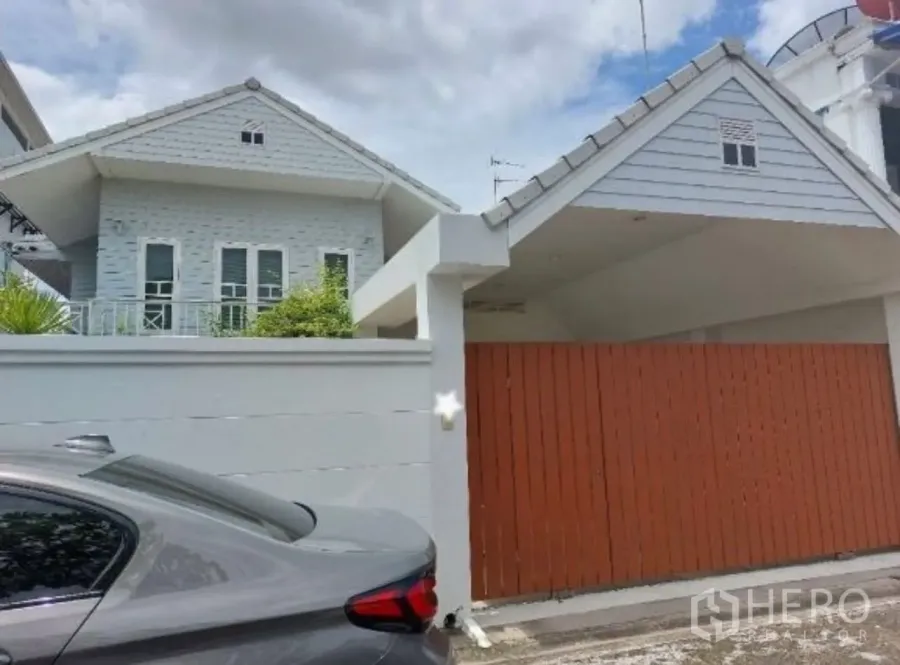 Detached House for rent in Suan Luang, Bangkok - Gable‑roof detached house exterior with a high white wall and wooden sliding gate in Suan Luang, Bangkok.