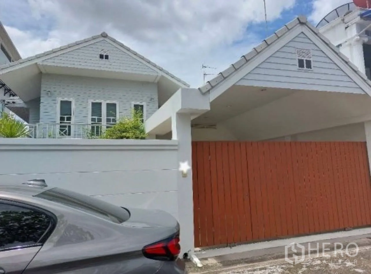 Detached House for rent in Suan Luang, Bangkok - Gable‑roof detached house exterior with a high white wall and wooden sliding gate in Suan Luang, Bangkok.