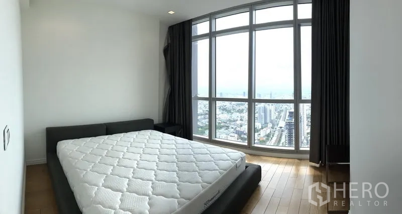 Condominium for rent or sale in Khlong San, Bangkok - Master bedroom with floor-to-ceiling curved windows, king bed and panoramic city view.