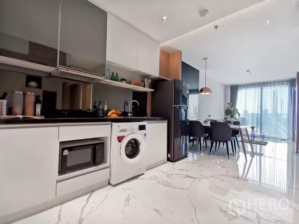 Condominium for rent in Watthana, Bangkok - Modern open‑plan kitchen with washing machine, black countertop and dining area opening to a balcony with city views.