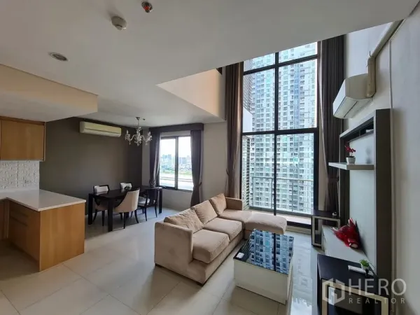 คอนโด ขายในRatchathewi, Bangkok - ห้องนั่งเล่นเพดานสูงพร้อมผนังกระจกเต็มบาน โซฟาสีเบจ ครัวเปิด และวิวเมือง