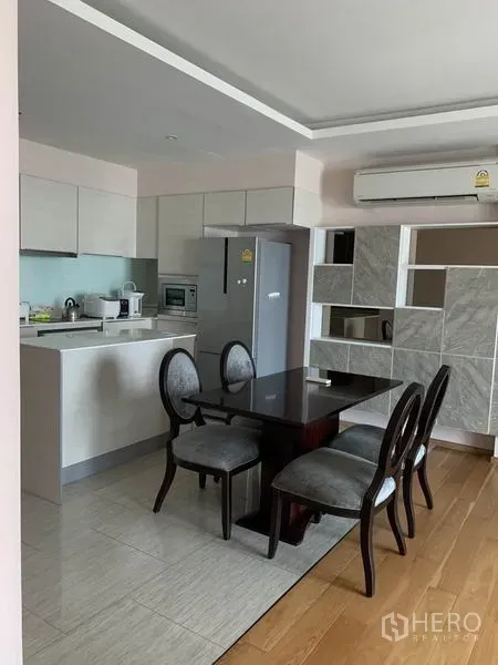 公寓 出租在Watthana, Bangkok - 曼谷公寓的开放式厨房，配白色橱柜、四人餐桌、冰箱和空调。