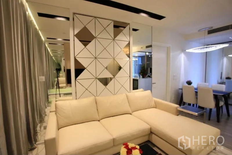 Condominium for rent or sale in Watthana, Bangkok - Lounge with L-shaped sofa, geometric feature wall and adjacent dining area.