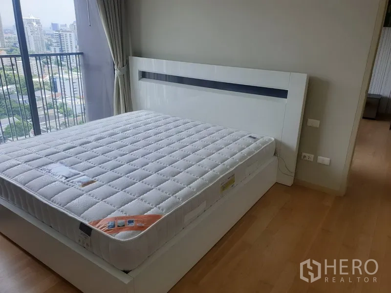 Condominium for rent in Watthana, Bangkok - Bedroom with large bed, light wood floors and balcony with city views.