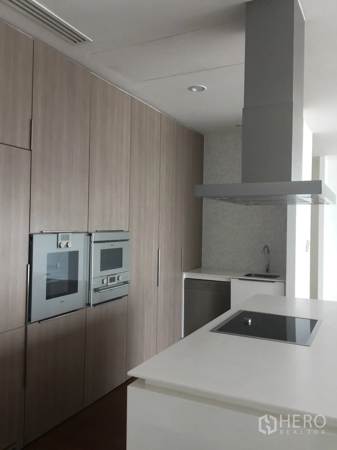 Condominium for rent in Pathum Wan, Bangkok - Modern kitchen with island, induction hob, twin built-in ovens and wood cabinetry.