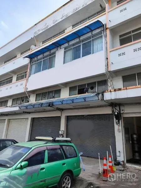 Shophouse for sale in Pathum Thani - Four-storey shophouse facade with blue awnings and roll-up shutters.