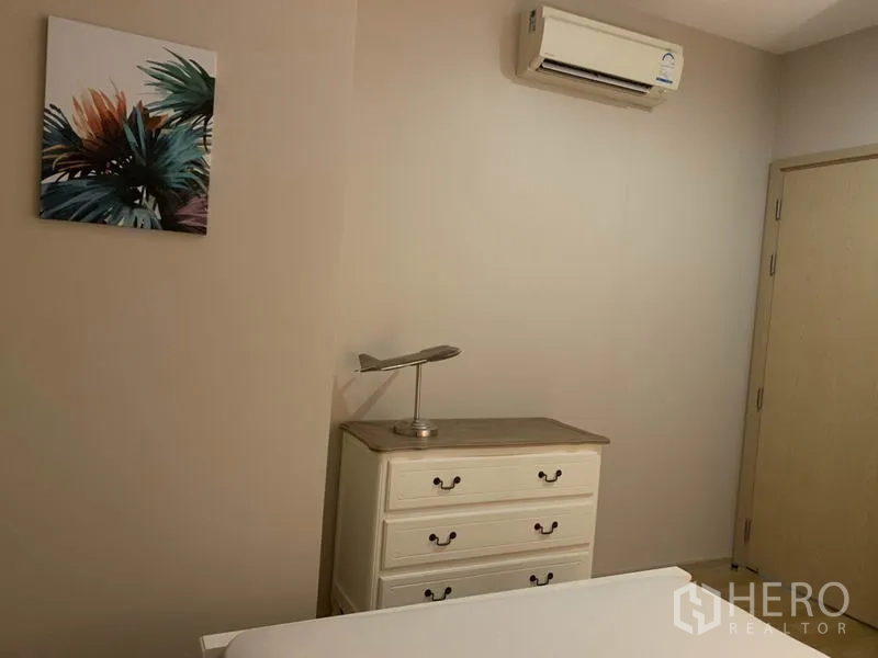 คอนโด ให้เช่าในWatthana, Bangkok - มุมห้องนอนที่มีตู้ลิ้นชักสีขาว ภาพติดผนัง เครื่องปรับอากาศ และประตูไม้