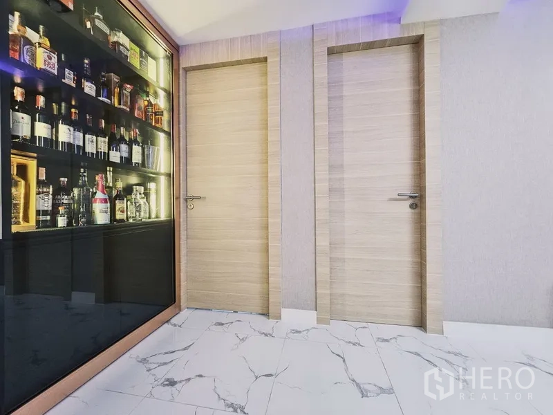 Condominium for sale in Bang Rak, Bangkok - Hallway with backlit liquor display cabinet and two light-wood doors on marble tiles.