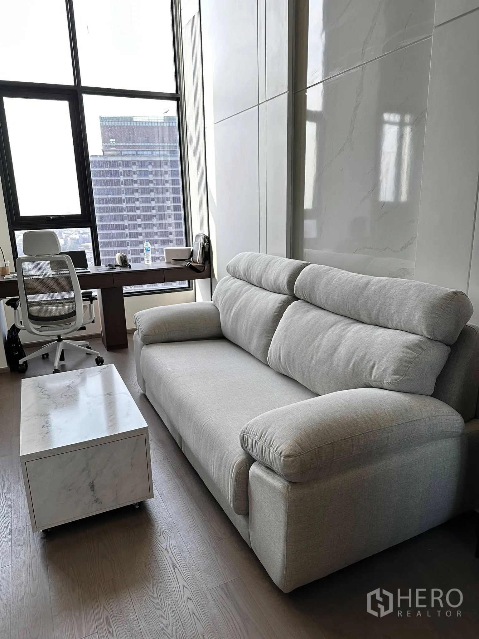 公寓 出租在Bang Rak, Bangkok - 采光充足的角落，灰色沙发与临窗书桌，眺望天际线。