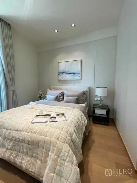 Condominium for rent in Pathum Wan, Bangkok - Secondary bedroom in soft neutral tones with bed, bedside table and artwork.